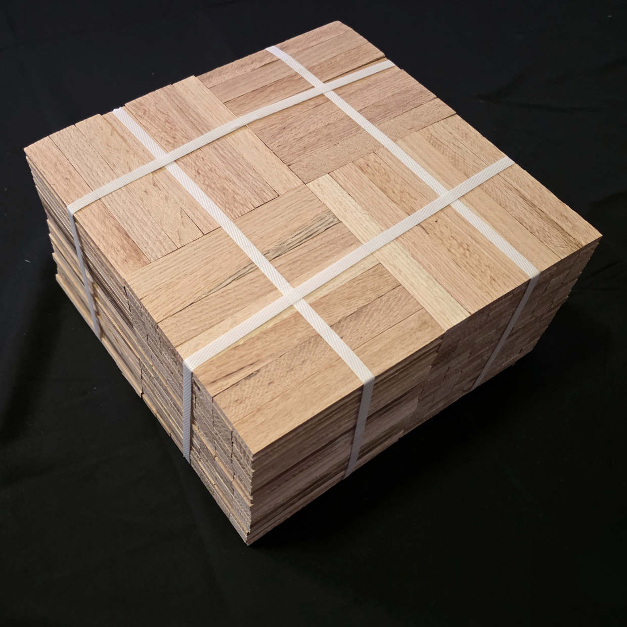 Unfinished parquet flooring with white straps intersecting near the corners. The background is black. There appears to be 20 parquet tiles in the bundle.