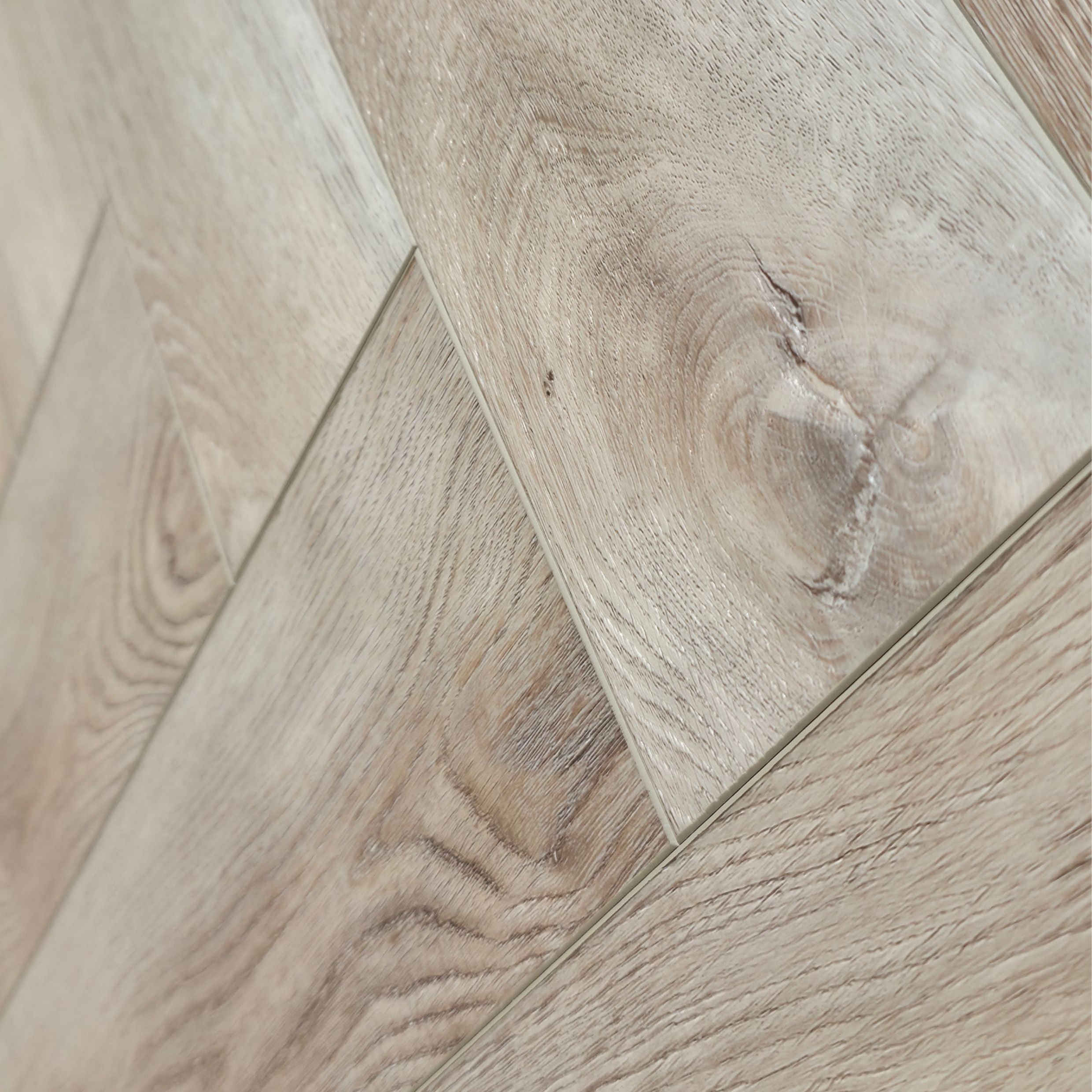 close up of light oak SPC herringbone flooring planks arranged in a diagonal pattern, showing natural wood grain and knots. Ancestral Drift - Herringbone is the product shown.