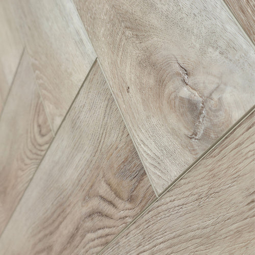 close up of light oak SPC herringbone flooring planks arranged in a diagonal pattern, showing natural wood grain and knots. Ancestral Drift - Herringbone is the product shown.