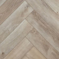 Light oak SPC herringbone flooring planks arranged in a diagonal pattern, showing natural wood grain and knots. Ancestral Drift - Herringbone is the product shown.