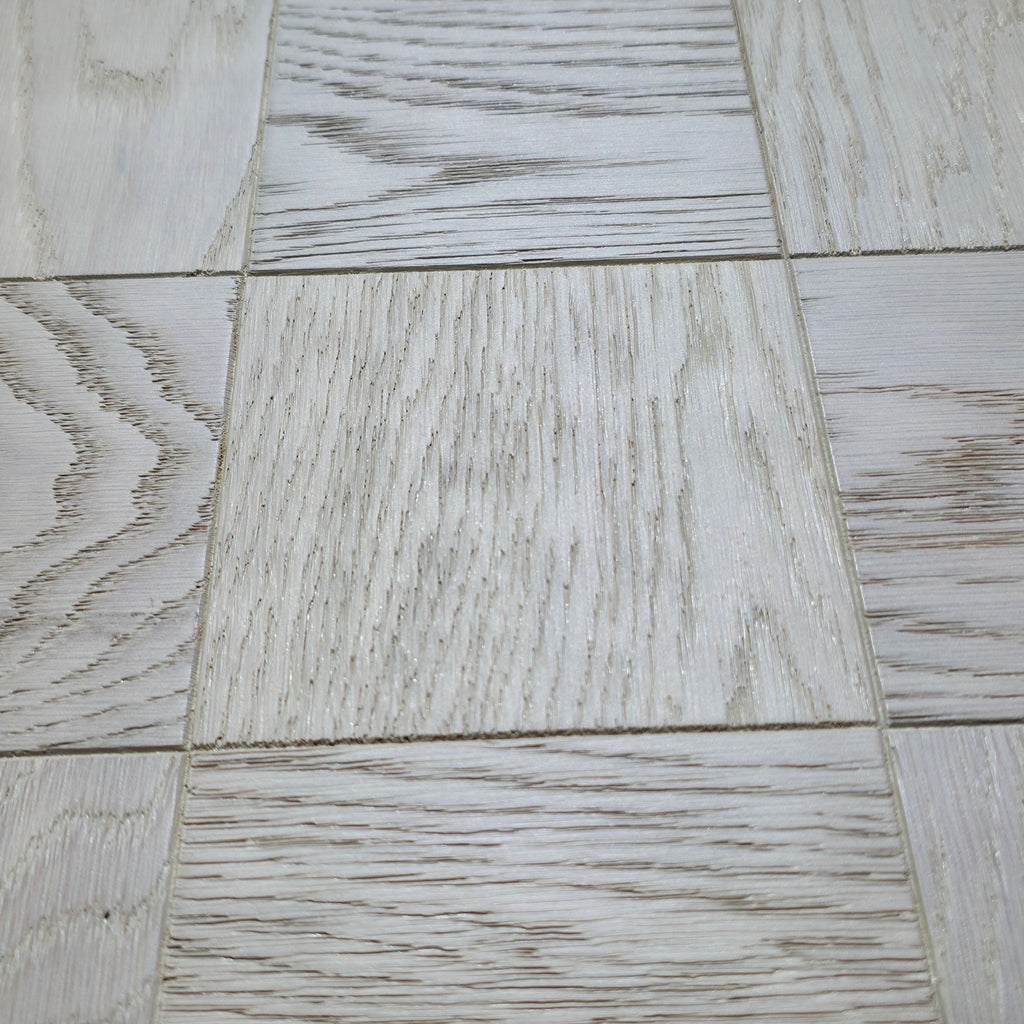 Light gray wood-look vinyl or laminate flooring tiles arranged in a grid pattern, showing various natural grain textures. Engineered European Oak Loire Mist Parquet flooring.