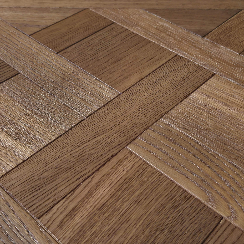 Close-up of a parquet wood floor with a herringbone pattern, showing natural brown wood grain texture. Engineered European Oak Vieux Manoir - Parquet shown.