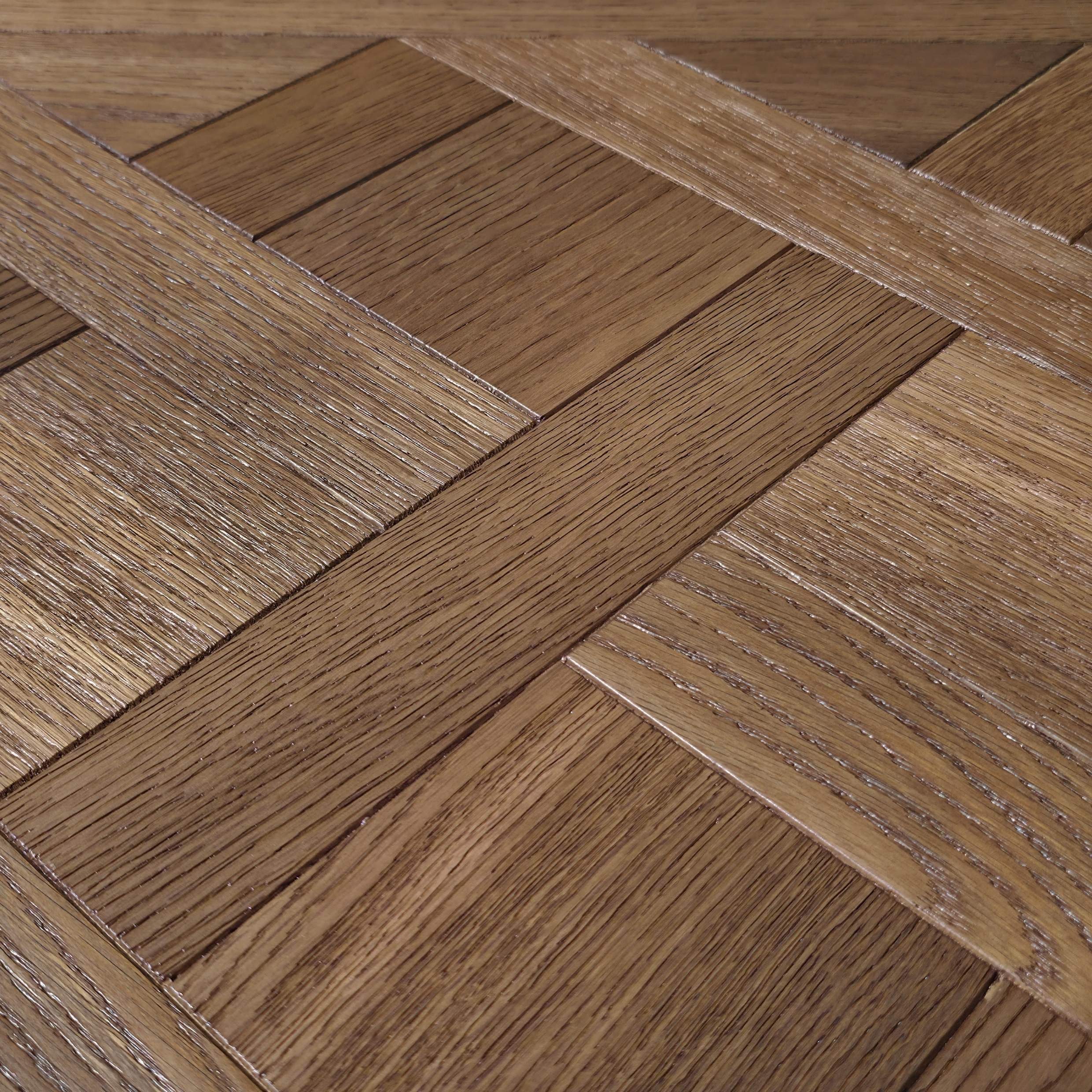 Close-up of a parquet wood floor with a herringbone pattern, showing natural brown wood grain texture. Engineered European Oak Vieux Manoir - Parquet shown.