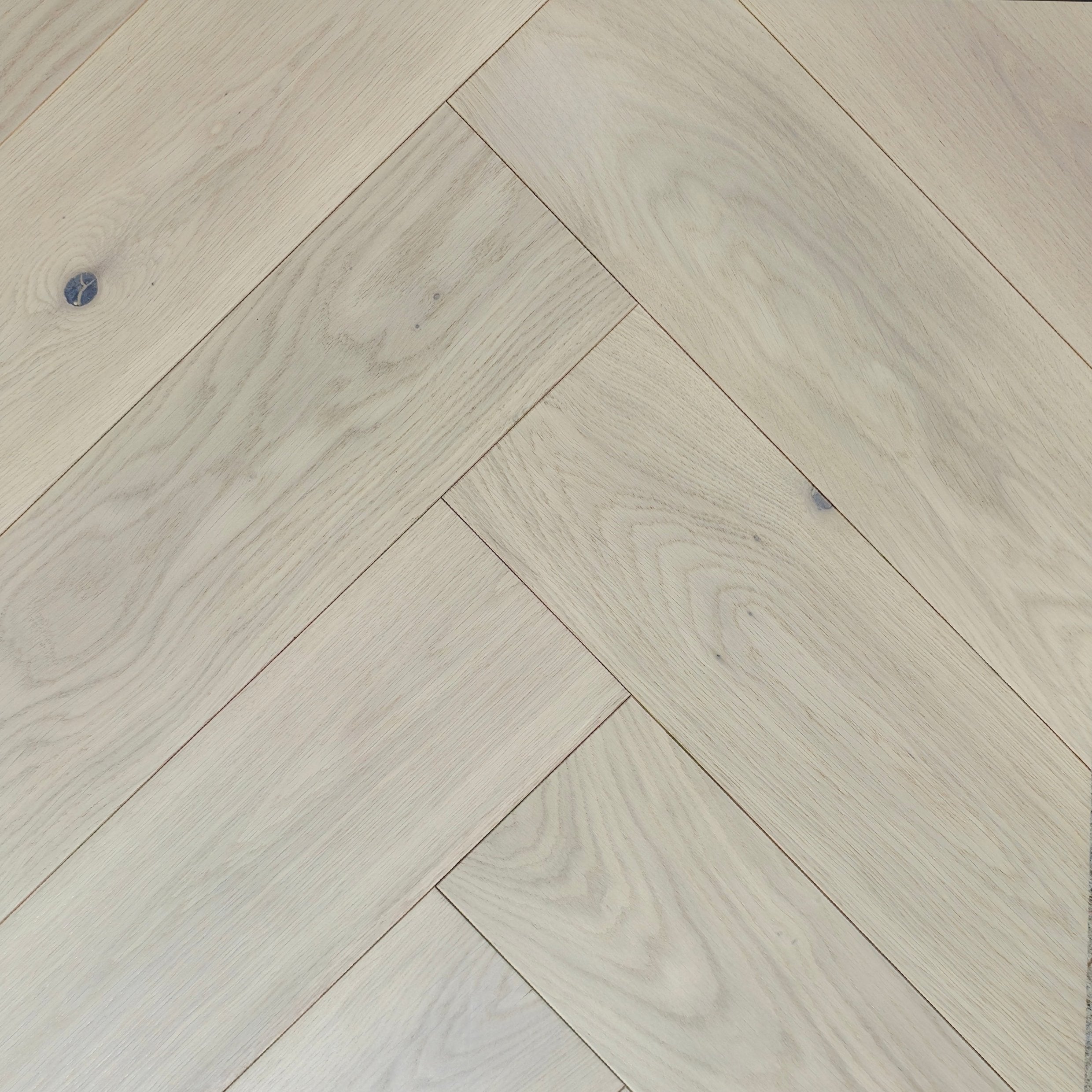 Light natural wood flooring planks arranged in a herringbone pattern, showing pale beige tones and subtle wood grain texture. Engineered European Oak Whistler Ascent - Herringbone
