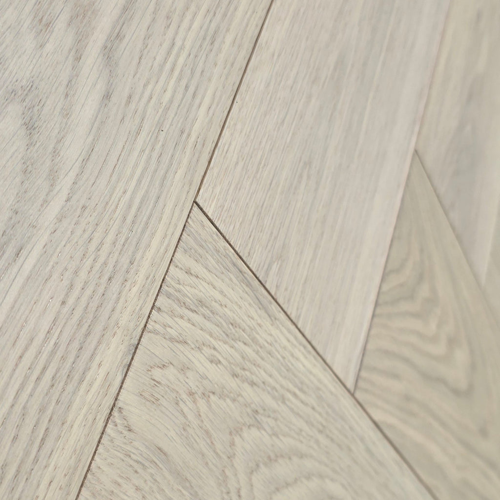Close-up of pale oak wood flooring planks arranged in a herringbone pattern, showing natural wood grain and light beige tones. Engineered European Oak Whistler Ascent - Herringbone