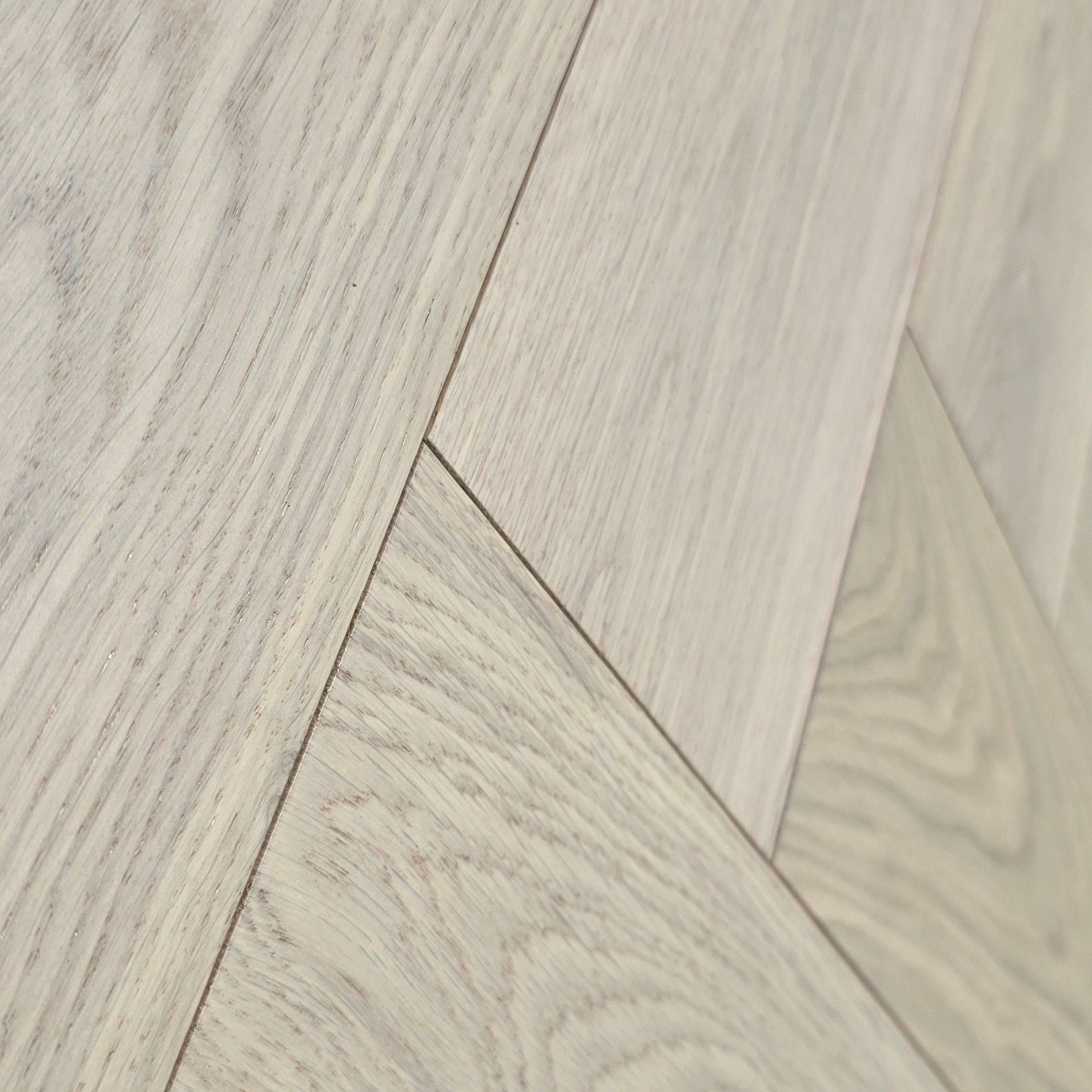 Close-up of pale oak wood flooring planks arranged in a herringbone pattern, showing natural wood grain and light beige tones. Engineered European Oak Whistler Ascent - Herringbone