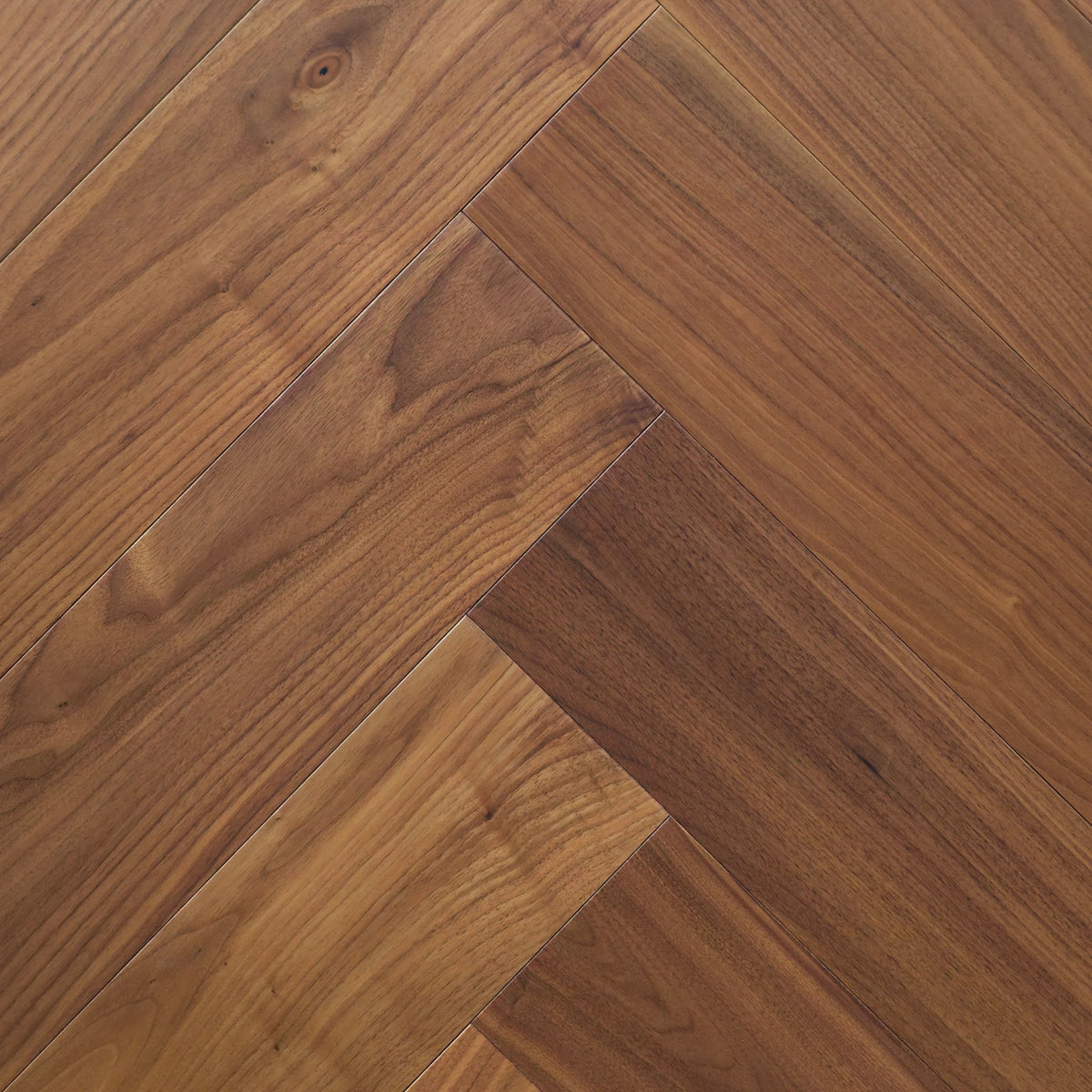 Herringbone pattern hardwood flooring planks in a warm medium brown wood finish with visible natural grain and knots. The product is Velours Noyer  - Herringbone