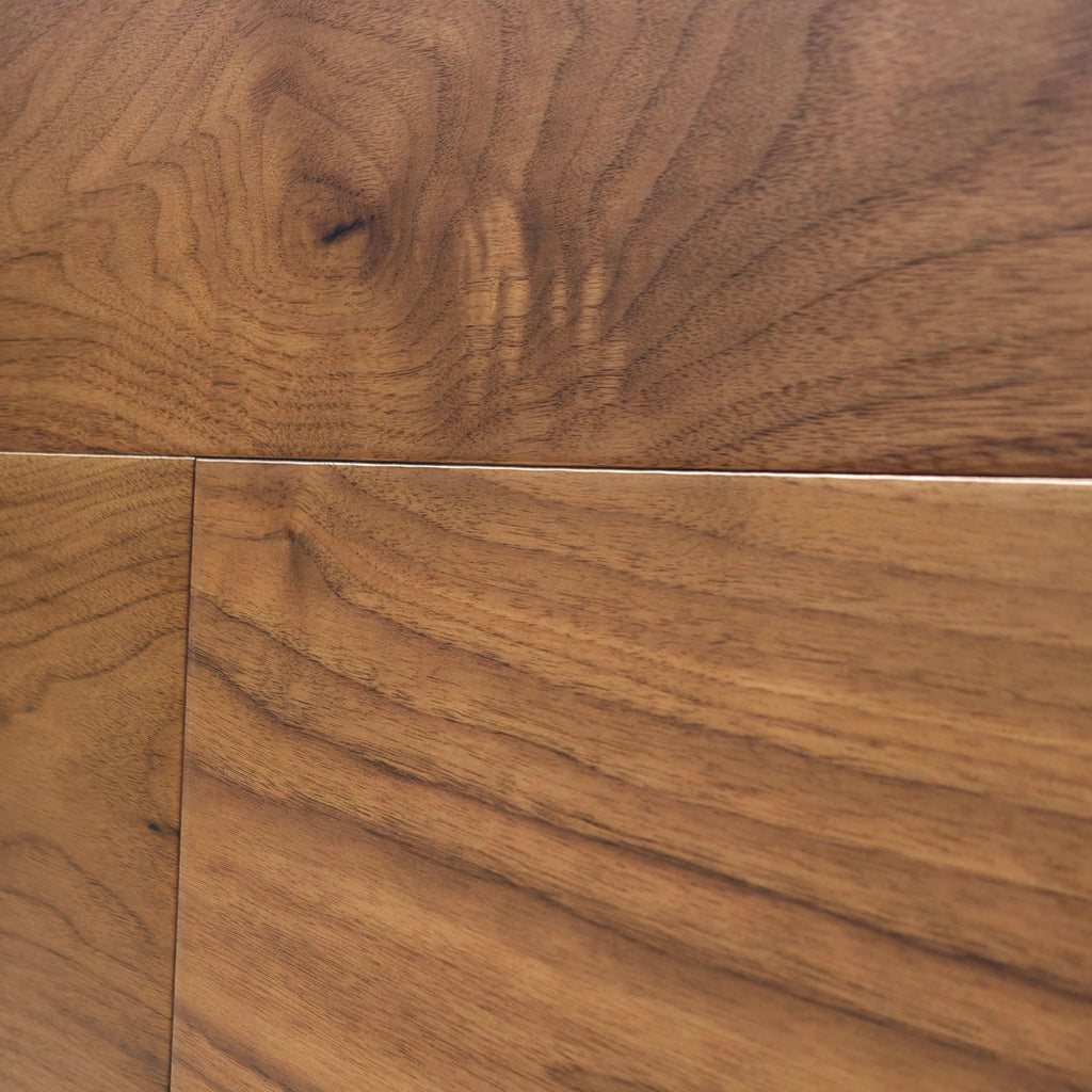 Close-up of warm medium-brown Walnut wood grain flooring with visible wood knots and natural grain patterns. The image is of Velours Noyer - Wide Plank.