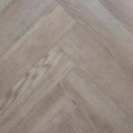 Light oak look herringbone SPC flooring planks arranged in a diagonal pattern, showing natural wood grain and subtle variations in tone. Image is of Geneva Mist - Herringbone