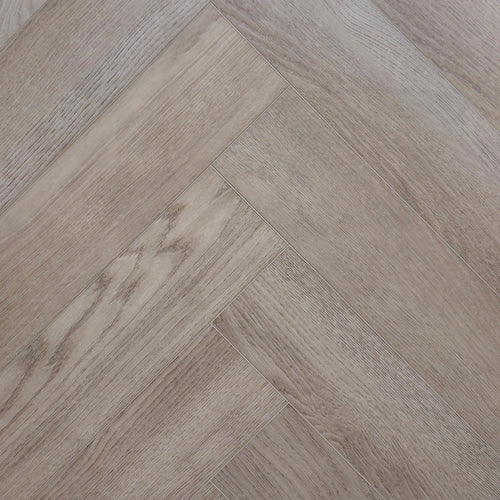 Light oak look herringbone SPC flooring planks arranged in a diagonal pattern, showing natural wood grain and subtle variations in tone. Image is of Geneva Mist - Herringbone