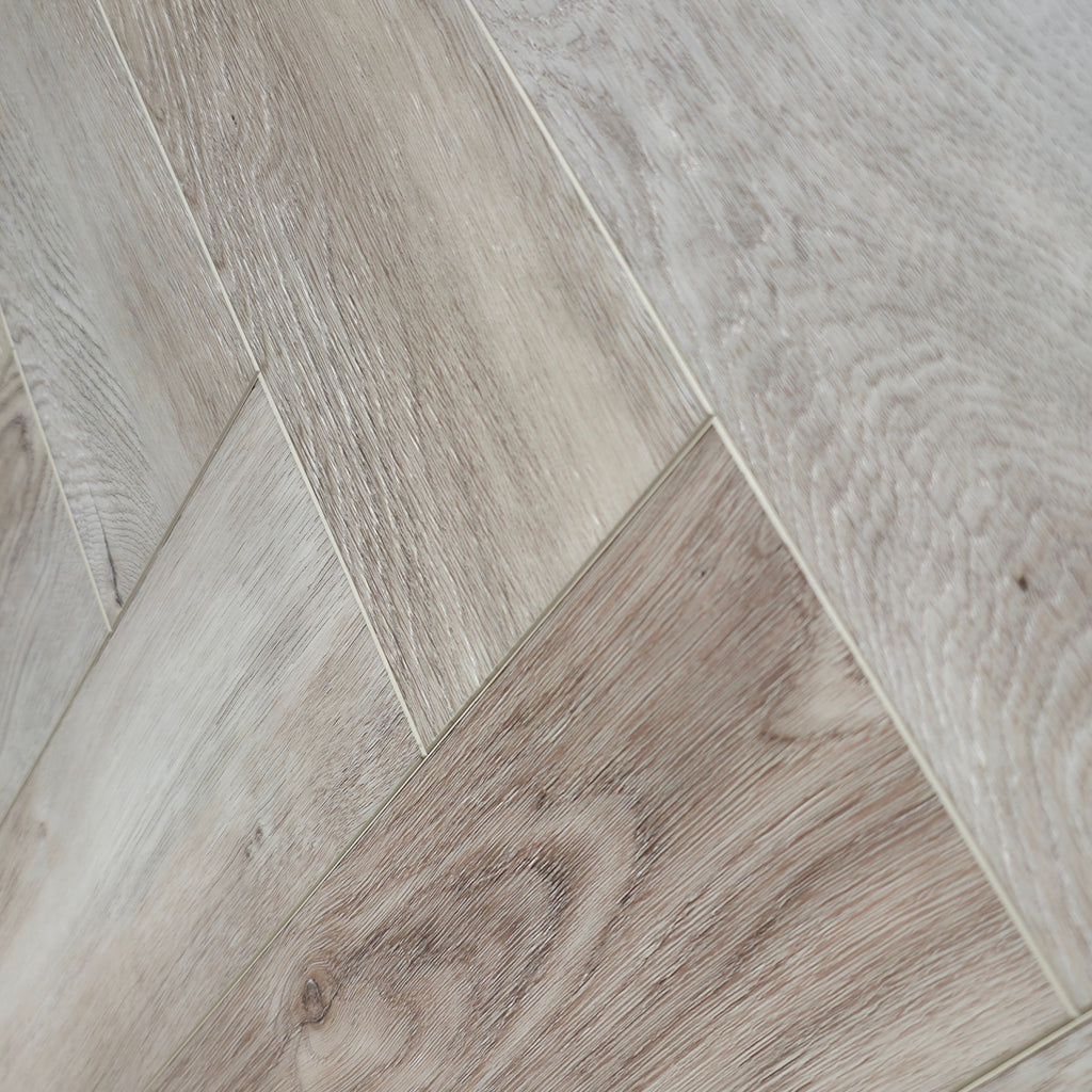 Light oak wood-look flooring planks arranged in a herringbone pattern, showing natural grain and subtle tonal variation. the image is a close up of Highland Ore - Herringbone