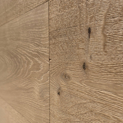 Close-up of light oak wood flooring planks showing natural grain patterns and knots. The flooring shown is engineered European oak Gstaad Glow Wide plank. 