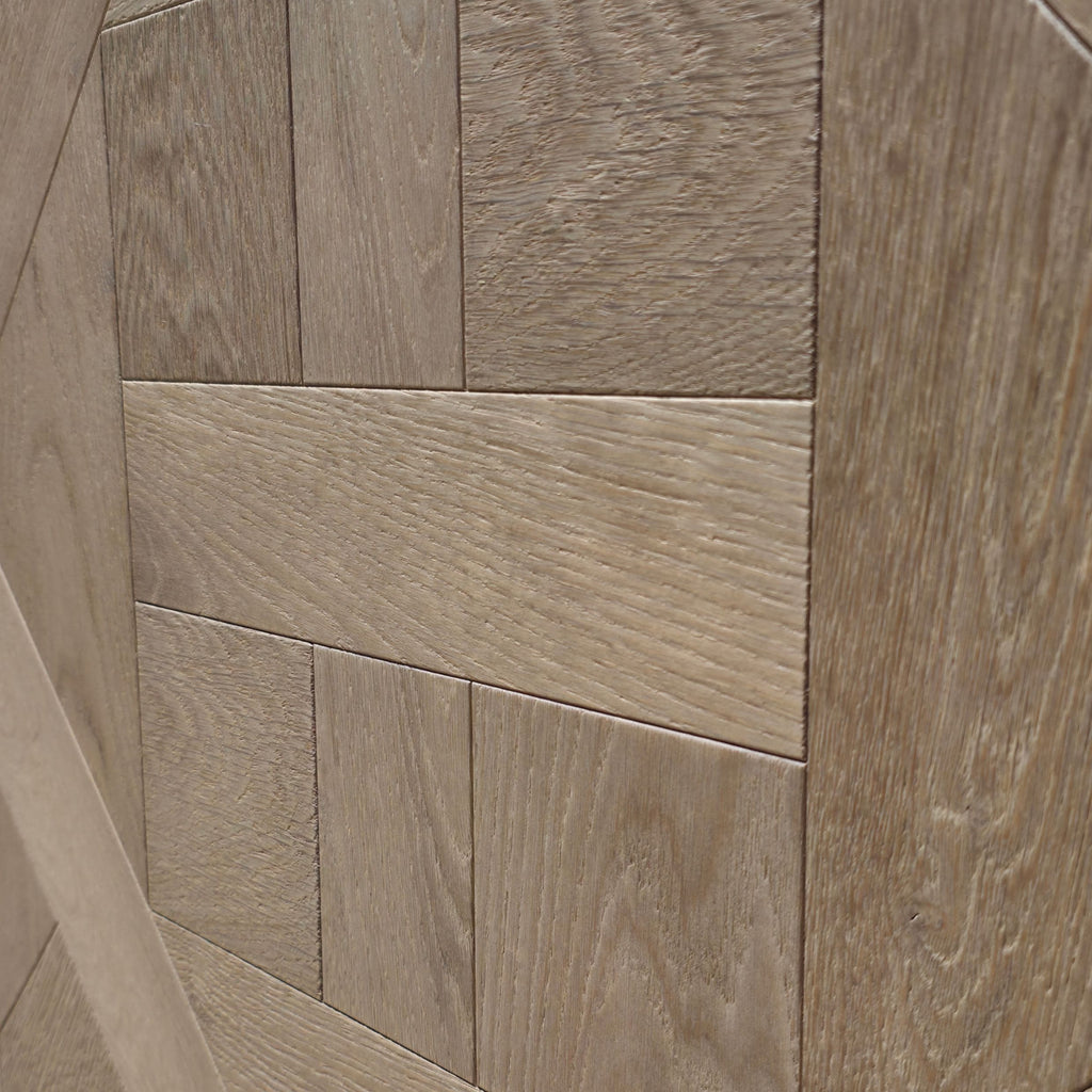 Close-up of light European white oak wood rectangular tiles arranged in a herringbone pattern, showing natural wood grain texture. Engineered European oak ember valley parquet tile shown. 