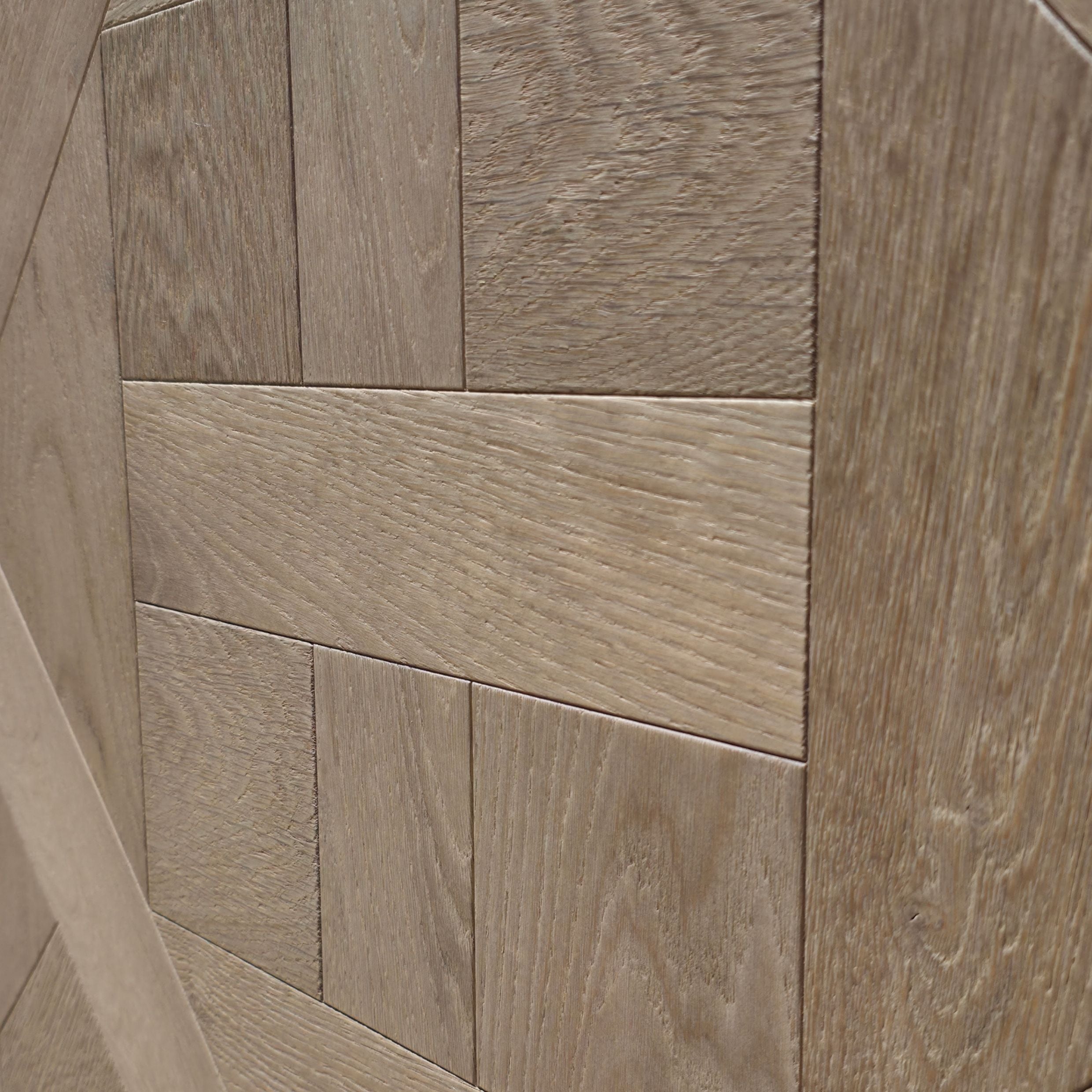 Close-up of light European white oak wood rectangular tiles arranged in a herringbone pattern, showing natural wood grain texture. Engineered European oak ember valley parquet tile shown. 