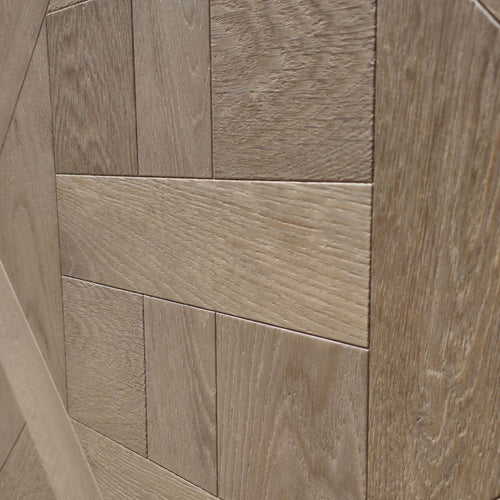 Close-up of light European white oak wood rectangular tiles arranged in a herringbone pattern, showing natural wood grain texture. Engineered European oak ember valley parquet tile shown. 