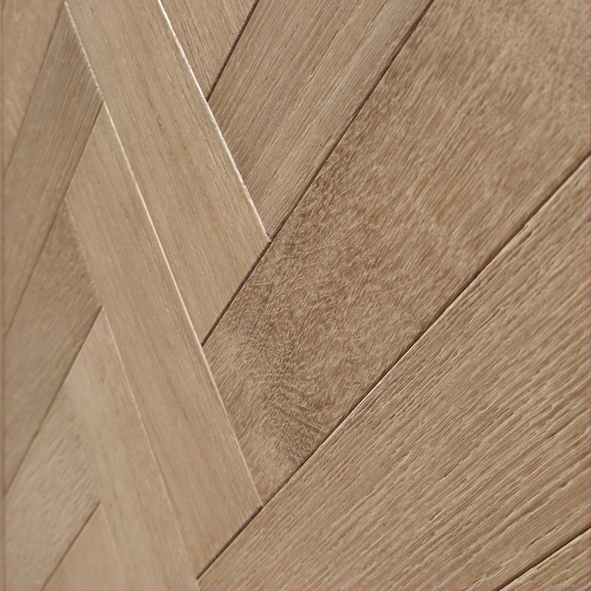 Close-up of light oak wood planks arranged in a herringbone pattern, showing natural wood grain and warm beige-brown tones. engineered European oak hearthside Oak parquet is shown.